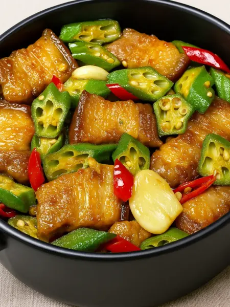 Easy Stir Fried Pork Belly Recipe with Okra Stir fried pork belly recipe with green okra, red chili slices, and whole garlic cloves in a savory sauce, presented in a black serving bowl.