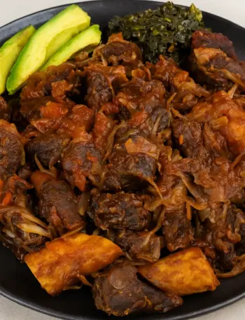 Best Ugandan Pork Stir Fry (Kikalayi Pork) Ugandan-style pork stir fry, also known as Kikalayi pork, served with matooke, avocado slices, and cabbage on a black tray.