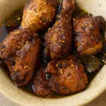Juicy adobo chicken recipe featuring chicken simmered in glossy brown sauce with garlic, pepper, and bay leaf garnish.