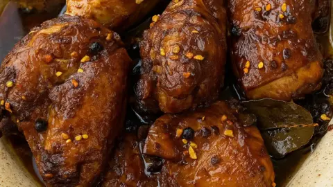 Juicy adobo chicken recipe featuring chicken simmered in glossy brown sauce with garlic, pepper, and bay leaf garnish.